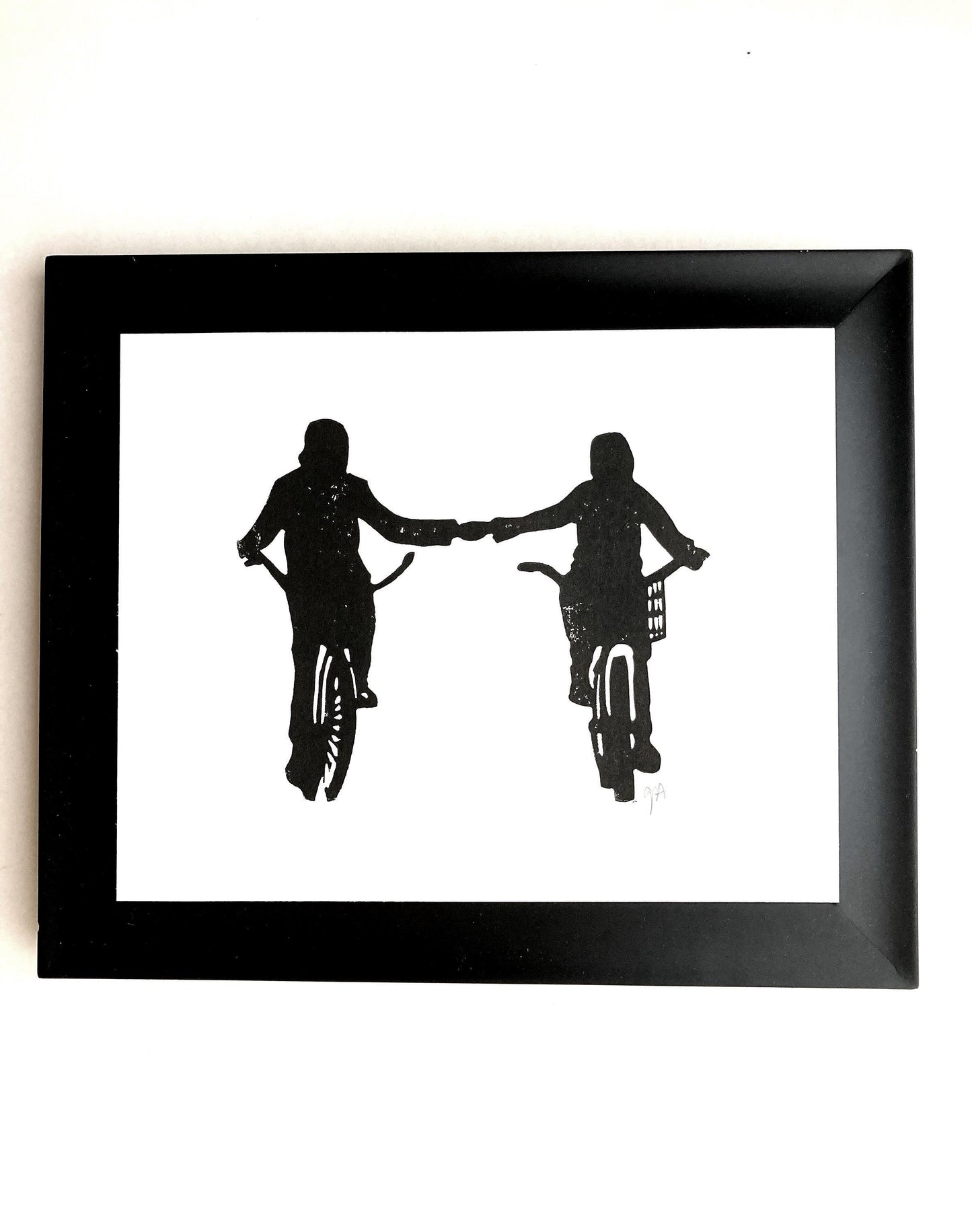 Framed black and white silhouette artwork of two people on bicycles holding hands.