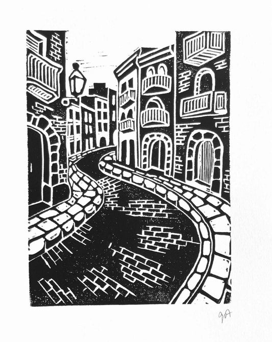 Black and white linocut print of cobblestone streets with buildings and a lamp post.