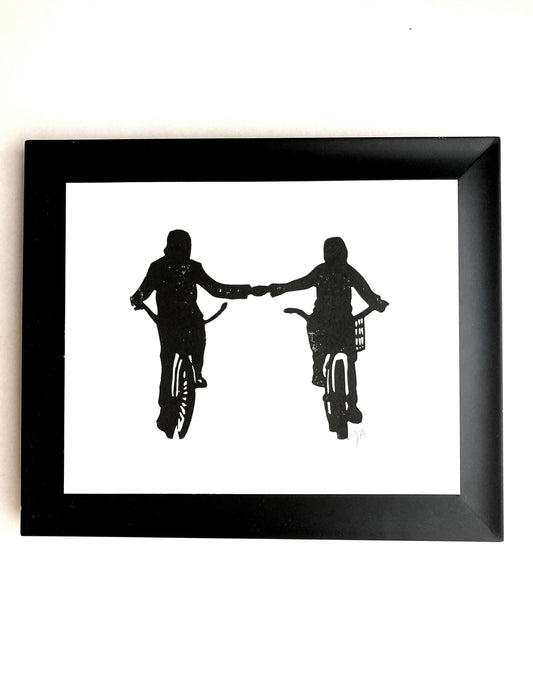 Framed black and white silhouette artwork of two people on bicycles holding hands.