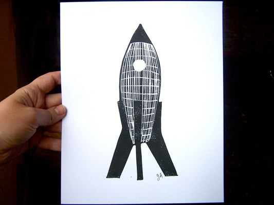 Hand holding a card with a black and white rocket illustration.