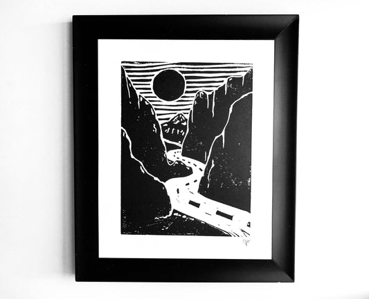 Framed black and white artwork of a mountain landscape with a road and sun.