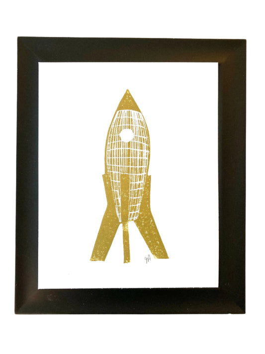 Framed artwork of a gold and white abstract rocketship on a white background