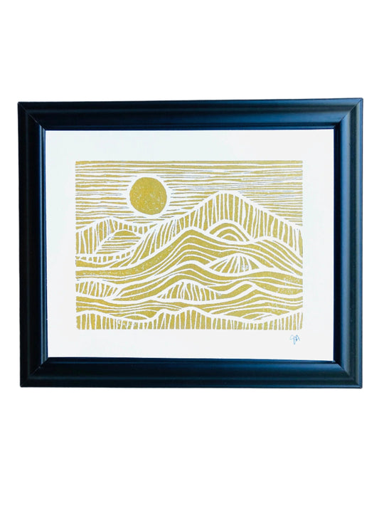 Framed linoleum block print of a mountain landscape with a sunset in metallic gold linocut ink